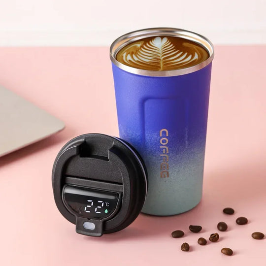 Blue insulated coffee tumbler with a digital temperature display on a pink surface with coffee beans.