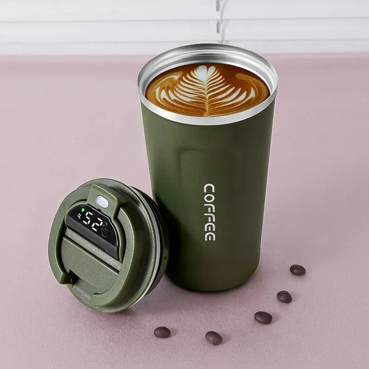 Green insulated coffee tumbler with a digital temperature display on a pink surface with coffee beans.