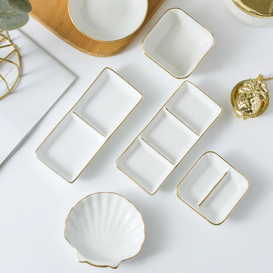 Set of white ceramic dishes with gold edges on a light surface.