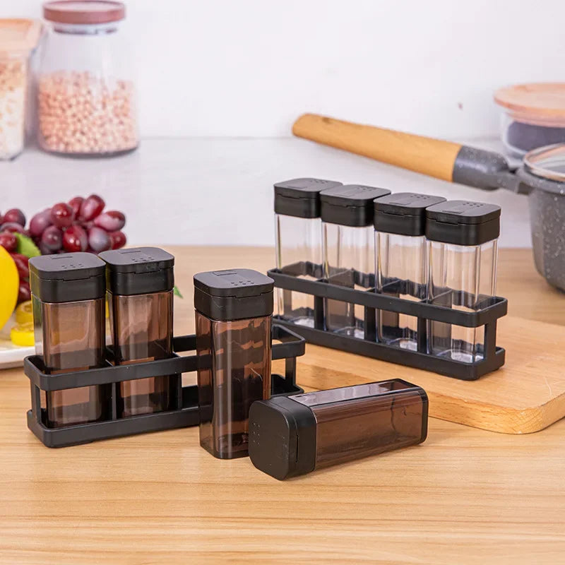 Set of transparent spice jars with black lids on a wooden surface.
