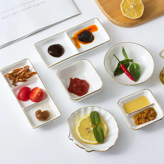 Set of small white dishes with gold rims containing various food items on a light surface.