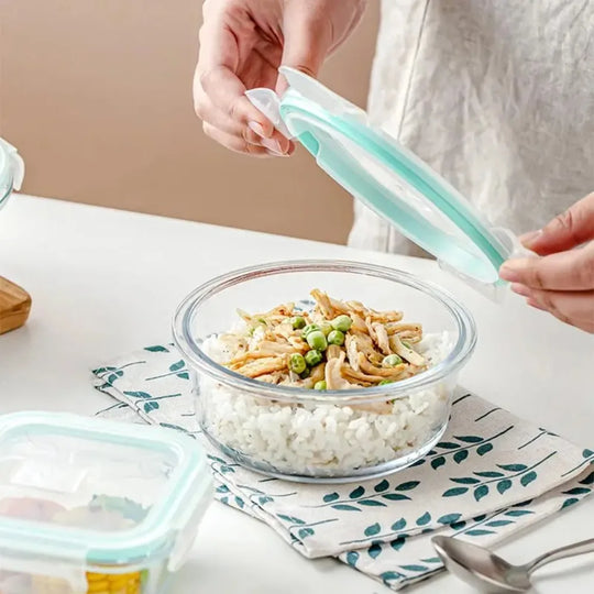 Person using a silicone lid to cover a glass bowl of food on a table.