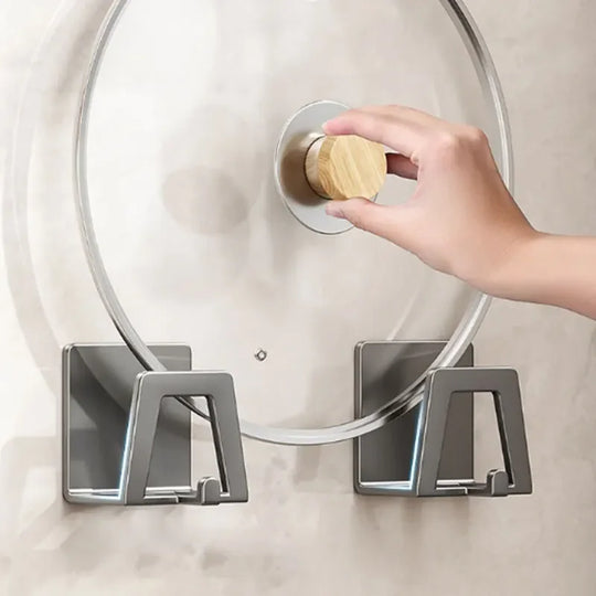 Hand using a wooden tool to open a glass lid with a metal handle on a neutral background