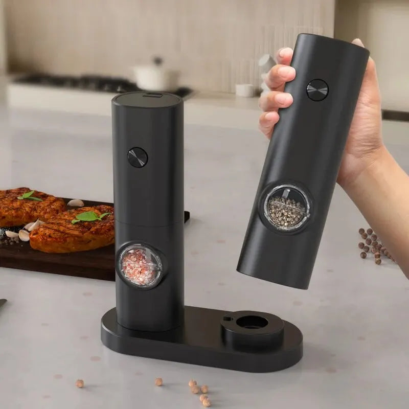 Black pepper grinder set on a kitchen counter with a hand holding one of the grinders.