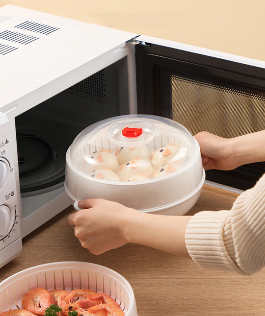 Person using a microwave steamer with food inside on a wooden surface.