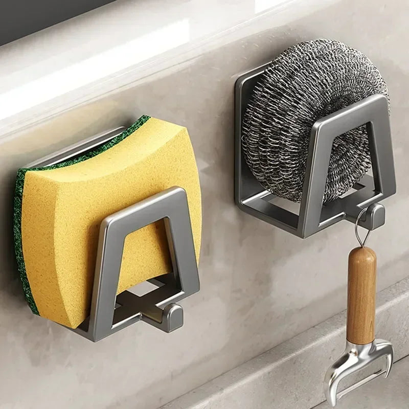 Wall-mounted kitchen sponge holder with yellow sponge, scrubber, and metal hook on a tiled wall.