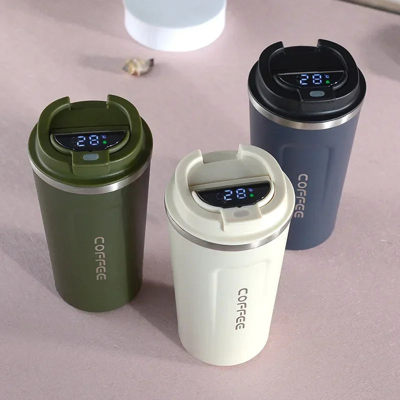 Three insulated coffee cups with digital temperature displays on a light pink surface.